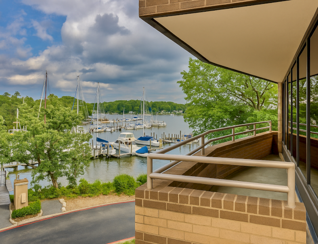 A balcony overlooking a marina with sailboats, surrounded by lush trees and under a partly cloudy sky, offering a serene water view.