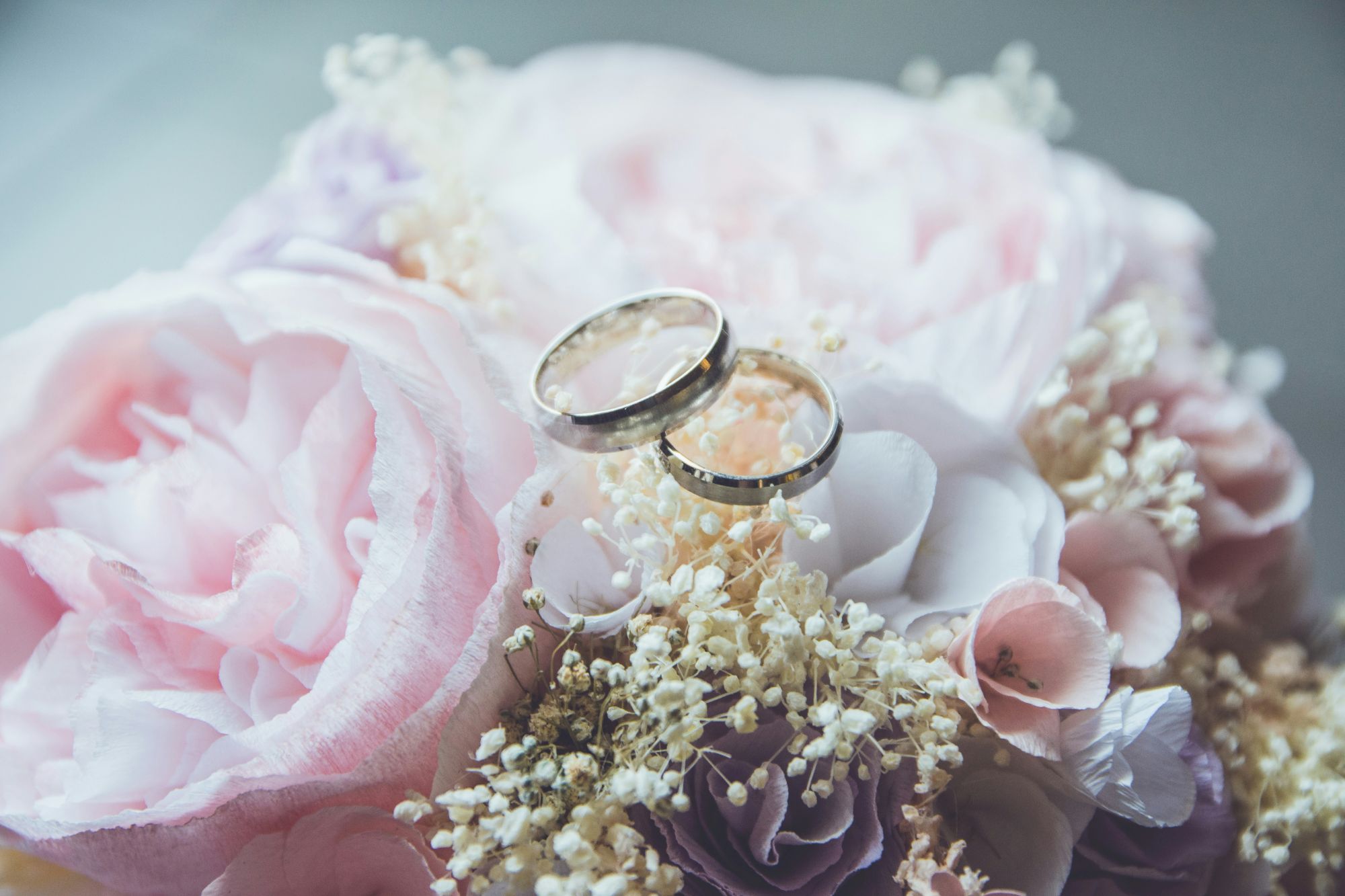 Two gold wedding rings rest on a bouquet of pink and white flowers, creating a romantic and elegant scene, perfect for a wedding.