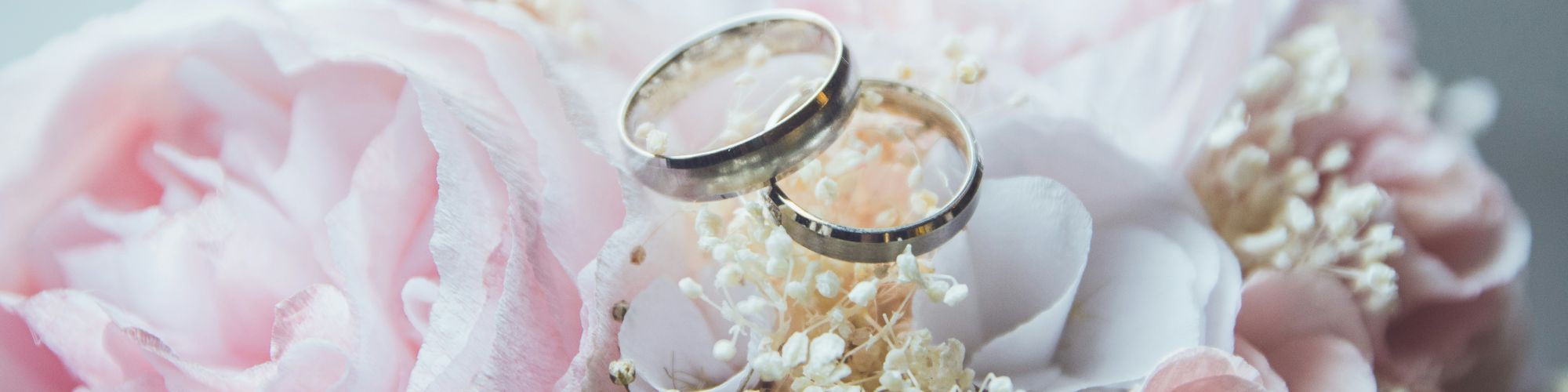 Two gold wedding rings rest on a bouquet of pink and white flowers, creating a romantic and elegant scene, perfect for a wedding.