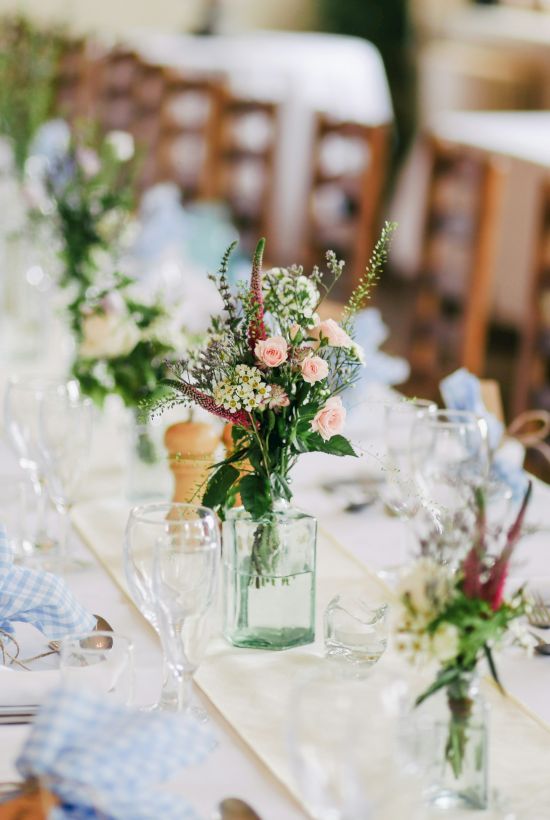 A beautifully decorated dining table, set with flowers, blue and white checkered napkins, glassware, and wooden chairs, ready for a formal event.