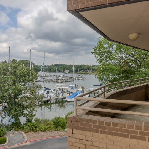 The image shows a view from a building balcony overlooking a marina with several docked boats and surrounding greenery, under a partly cloudy sky.