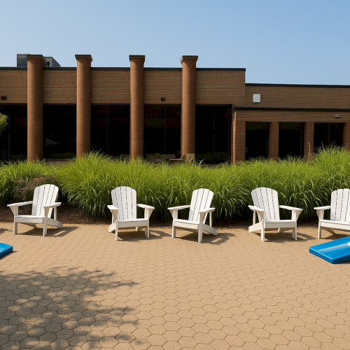 The image shows white Adirondack chairs and cornhole boards on a patio in front of a building with columns and greenery.