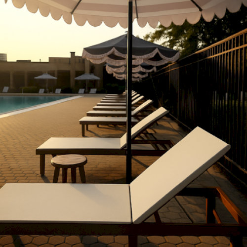 Poolside scene with a row of empty lounge chairs and umbrellas, adjacent to a pool, in soft evening light.