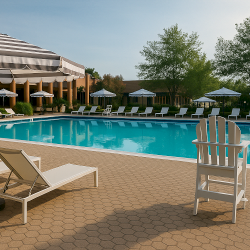 An outdoor pool area with lounge chairs, umbrellas, and greenery surrounding it under a clear sky.