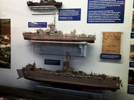 The image shows a display of three ship models mounted on a wall, along with descriptive plaques and a historical document related to the ships.