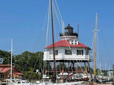 The image shows a marina with several boats docked and a distinctive, raised lighthouse structure with a red roof in the background.