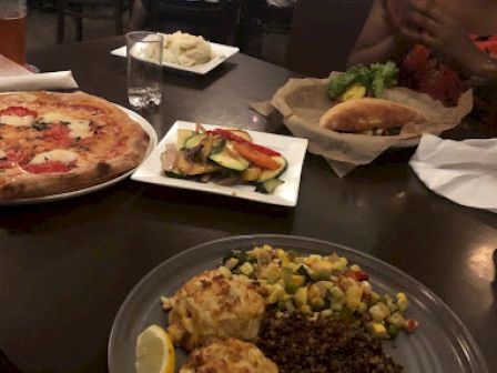 The image shows a dining table with various dishes, including a pizza, sandwiches, and a platter with rice, lemon wedges, and dipping sauces.