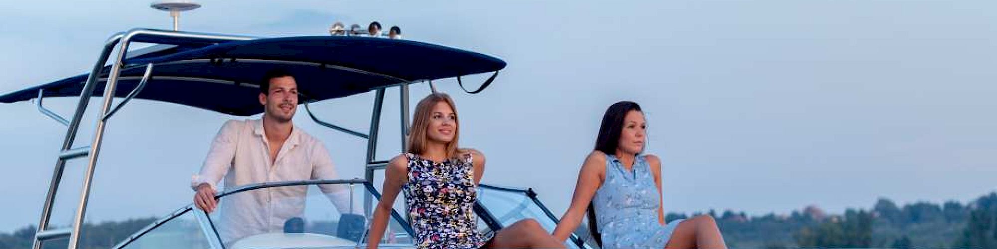Three people are enjoying a boat ride on a white yacht under a clear sky with a visible moon, and a distant shoreline in the background.